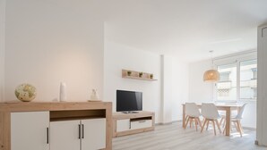 Et moderne, godt oplyst værelse med et træskrivebord, et fladskærms-tv, en globus og et spiseområde med hvide stole.