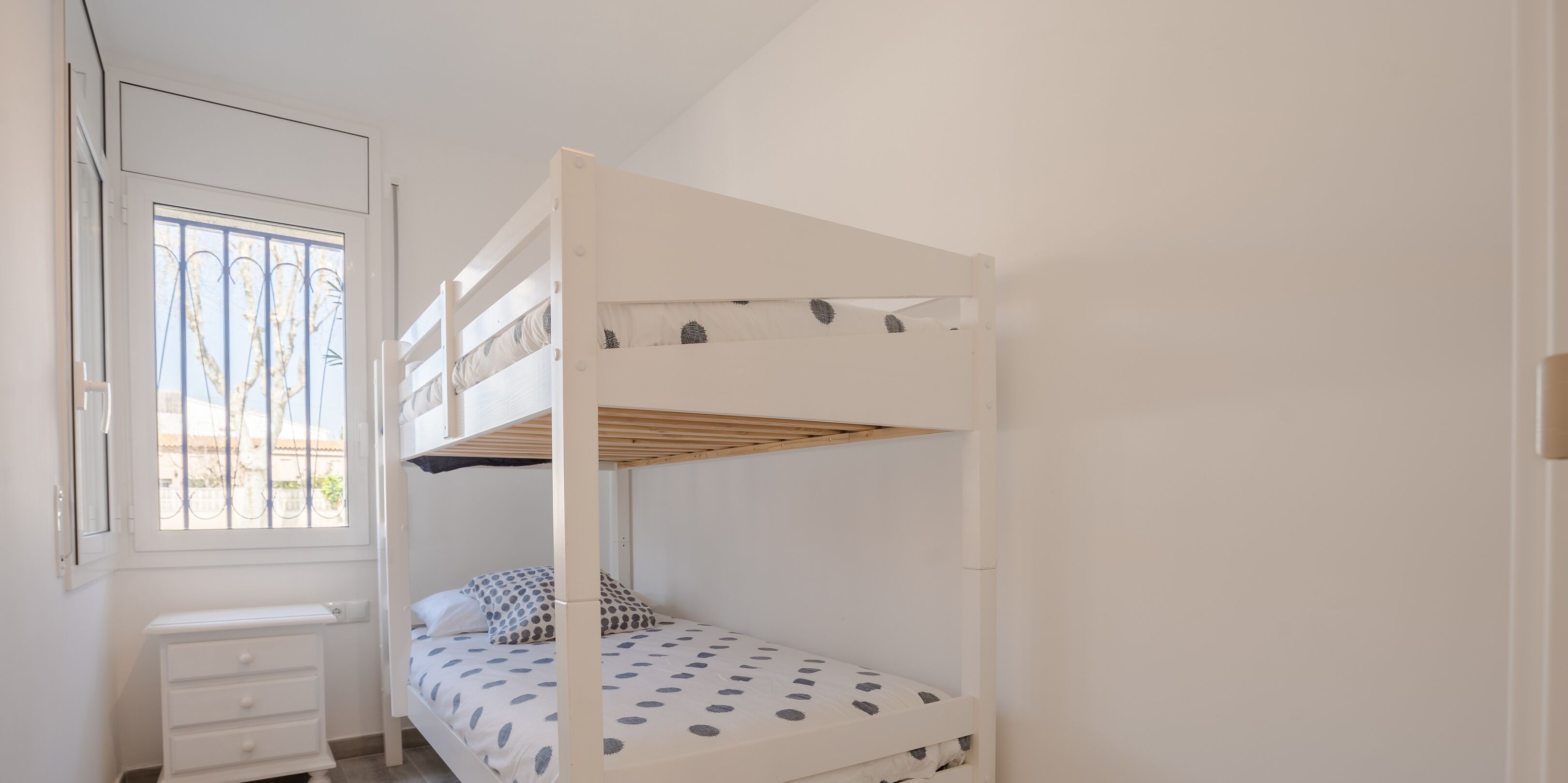 A bunk bed with a window, a small bedside table, and a polka dot bedspread.