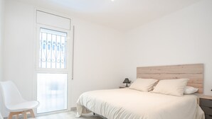 Et soveværelse med seng, natbord, lampe, stol og et vindue med udsigt.