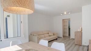 En moderne stue med et træspisebord, hvide stole, en beige sofa og en vævet lampe.
