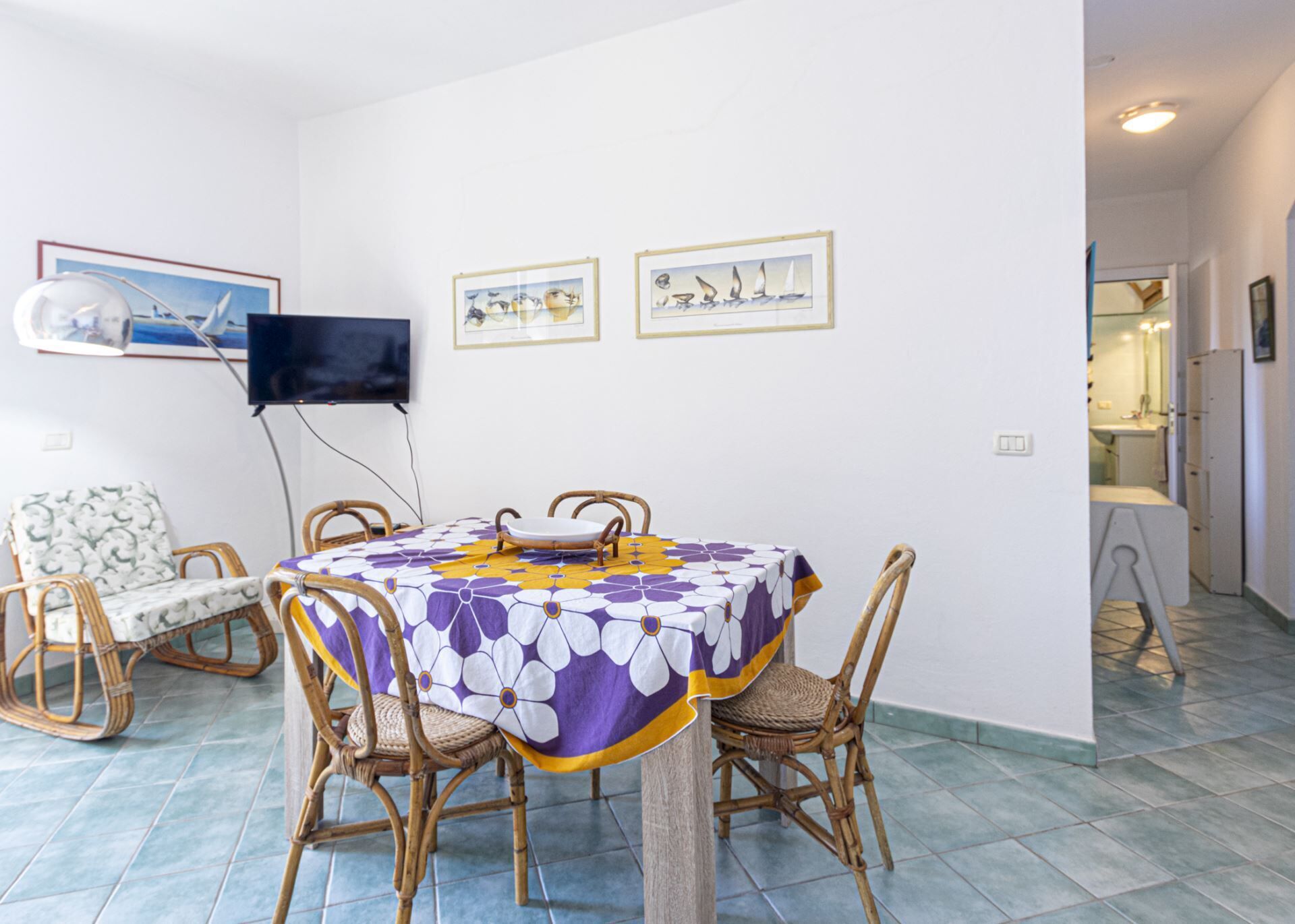Un coin repas avec une table ronde recouverte d’une nappe à motifs, entourée de chaises en osier.
