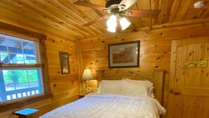 A wooden cabin bedroom with a bed, a ceiling fan, a window, and a door.