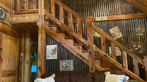 A wooden interior with a staircase, a brown leather couch, and a coffee table with books and a remote control.