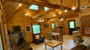 A cozy cabin interior with a stone fireplace, wooden furniture, and a high ceiling with exposed beams.