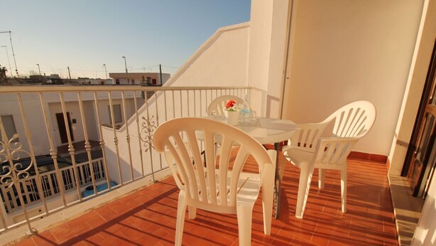 Un balcone con un tavolo bianco e due sedie bianche, una piccola pianta in vaso e vista sulla città.