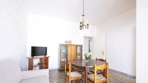 Zona pranzo con tavolo e sedie in legno, televisione su un mobile e pensile con ante in vetro.