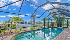 An indoor swimming pool with a glass ceiling, surrounded by palm trees and a view of houses.