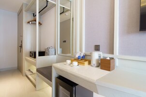 A modern hotel room with a kitchenette, a seating area with a coffee maker, and a mirror reflecting the room.