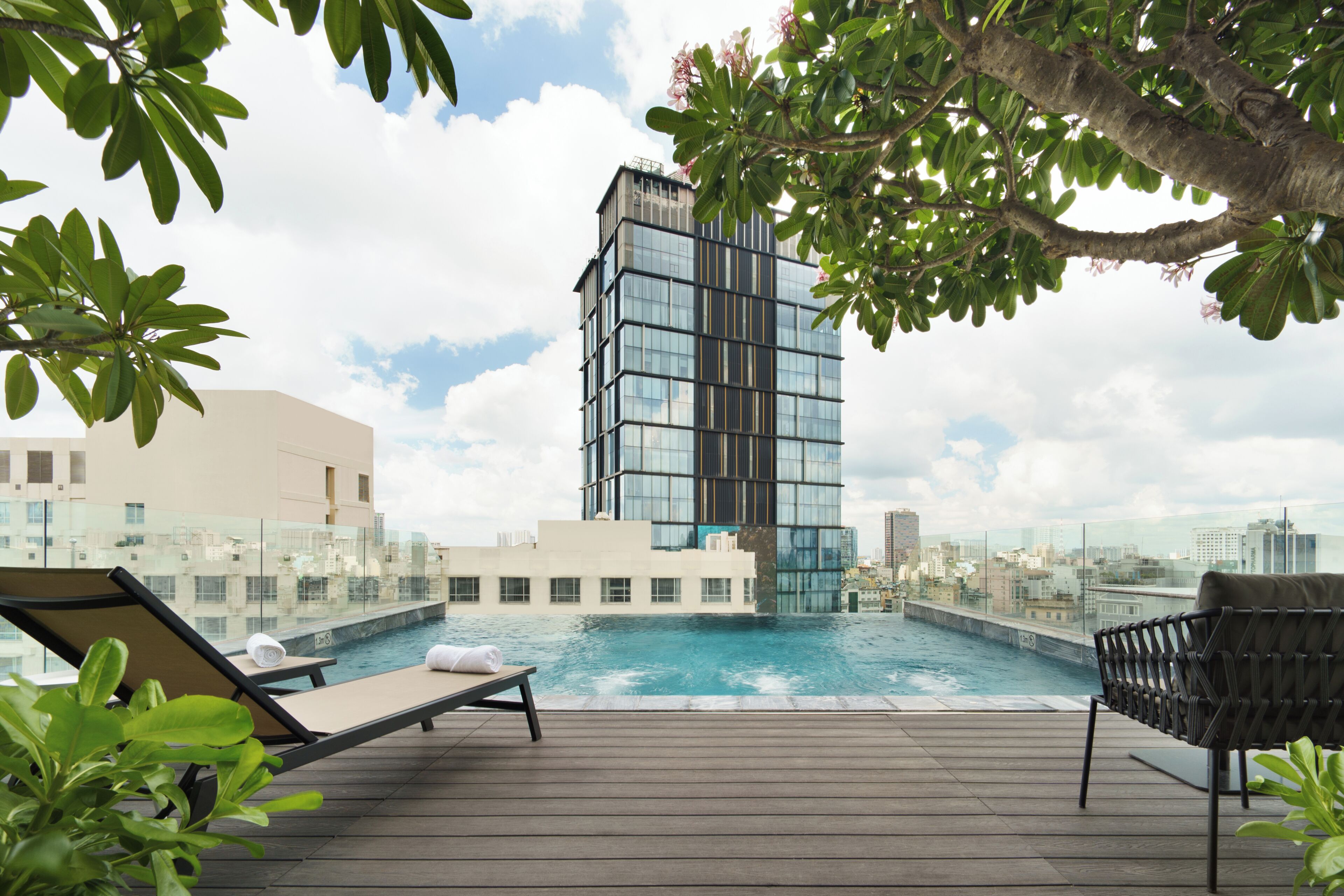 A rooftop pool area with lounge chairs, a glass barrier, and a modern building in the background.