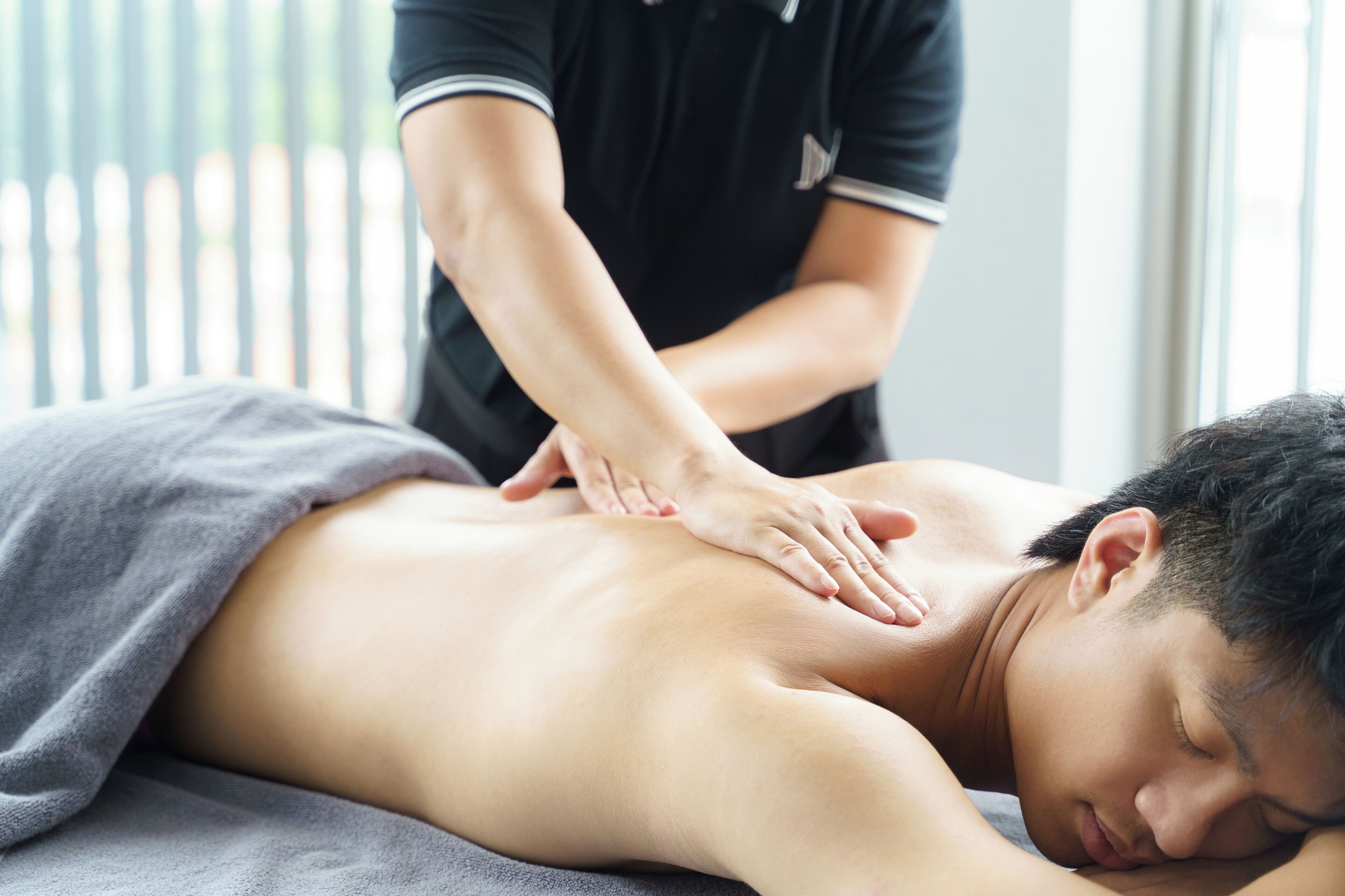 A person receiving a back massage in a room with a window and blinds.