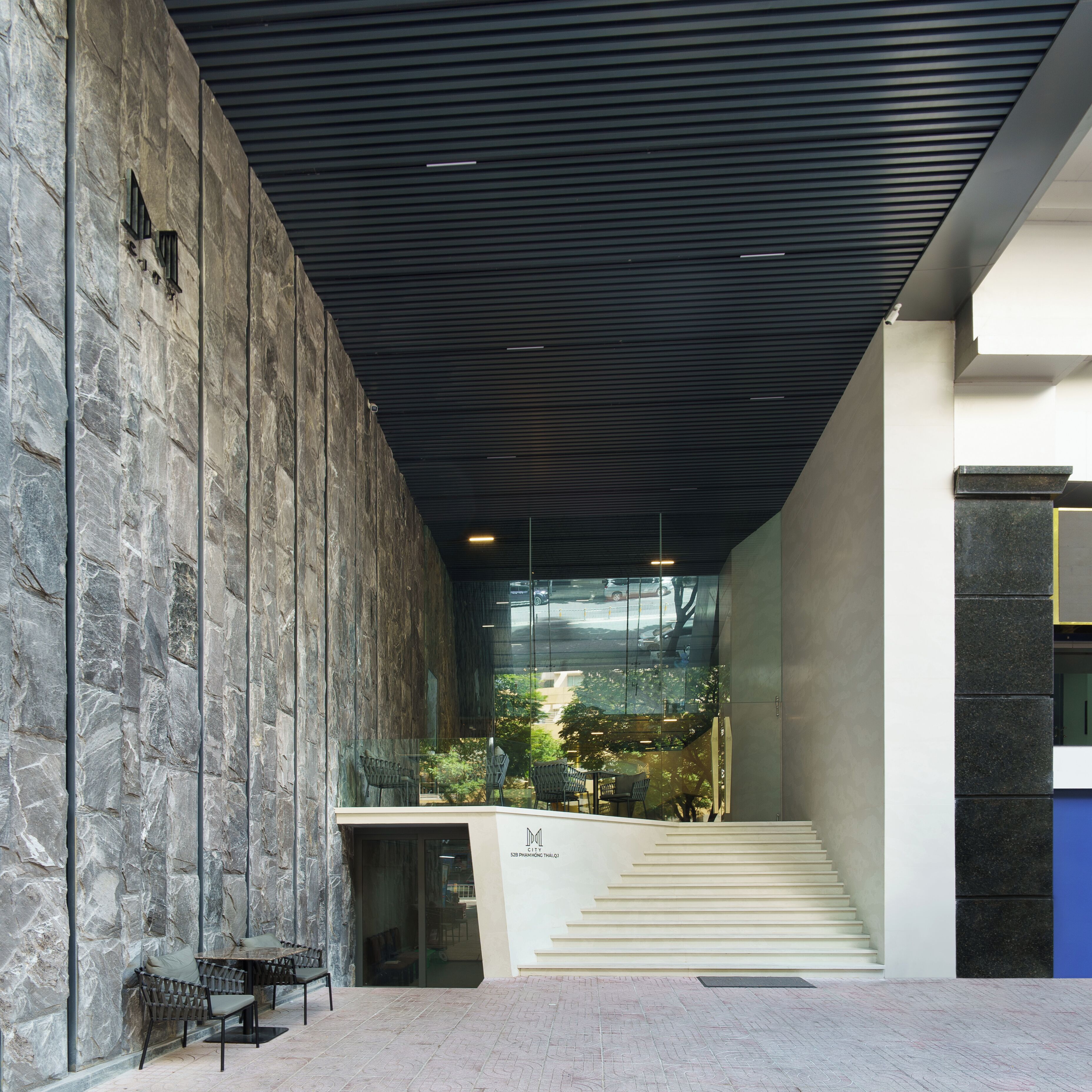 Un edificio moderno con fachada de piedra, una escalera y un área de descanso con sillas y una mesa.