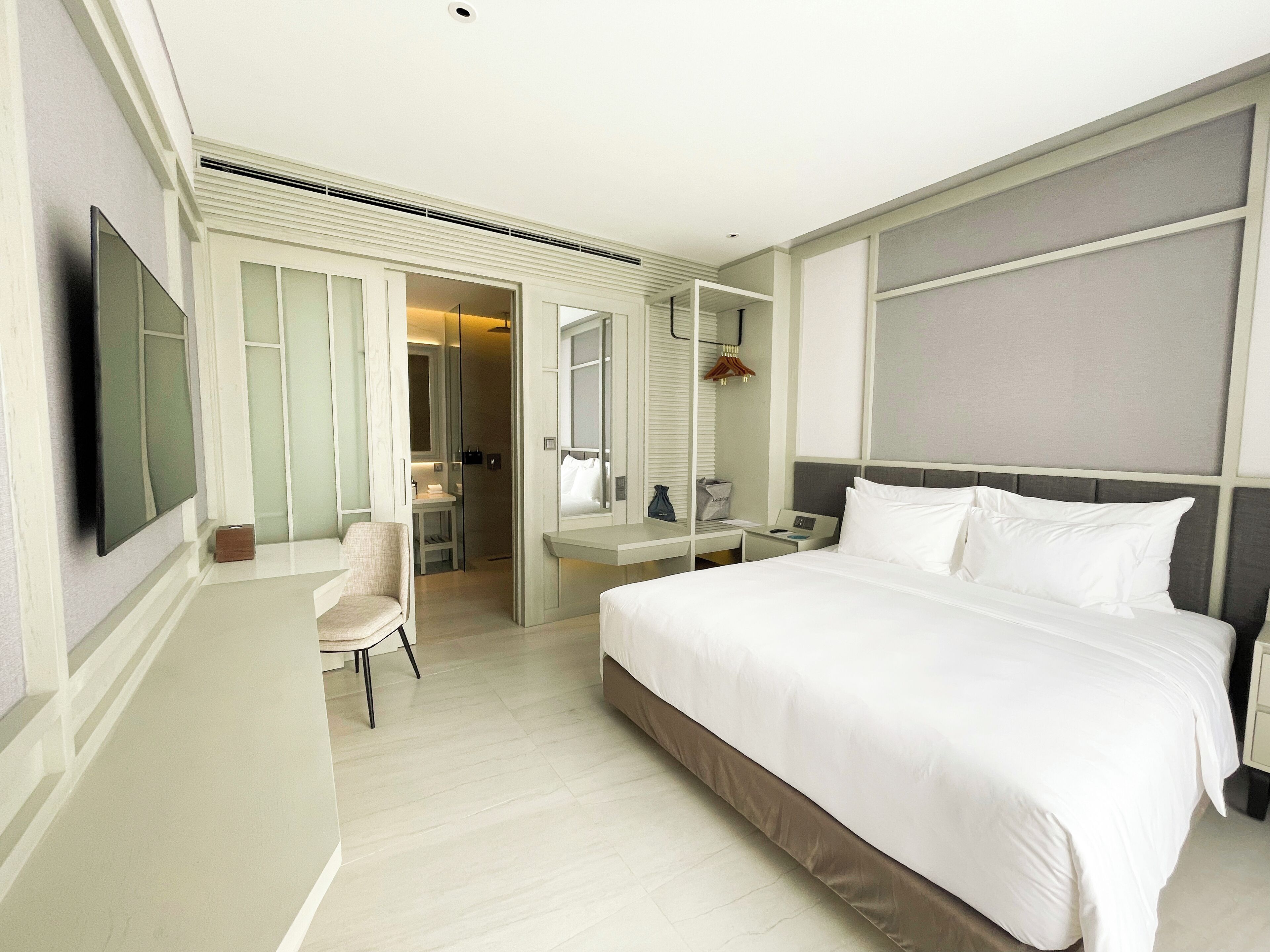 A hotel room with a large bed, a desk, a chair, a mirror, and a television.