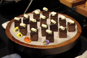 A dessert tray with chocolate brownies and decorative white chocolate rolls, accompanied by small flowers.