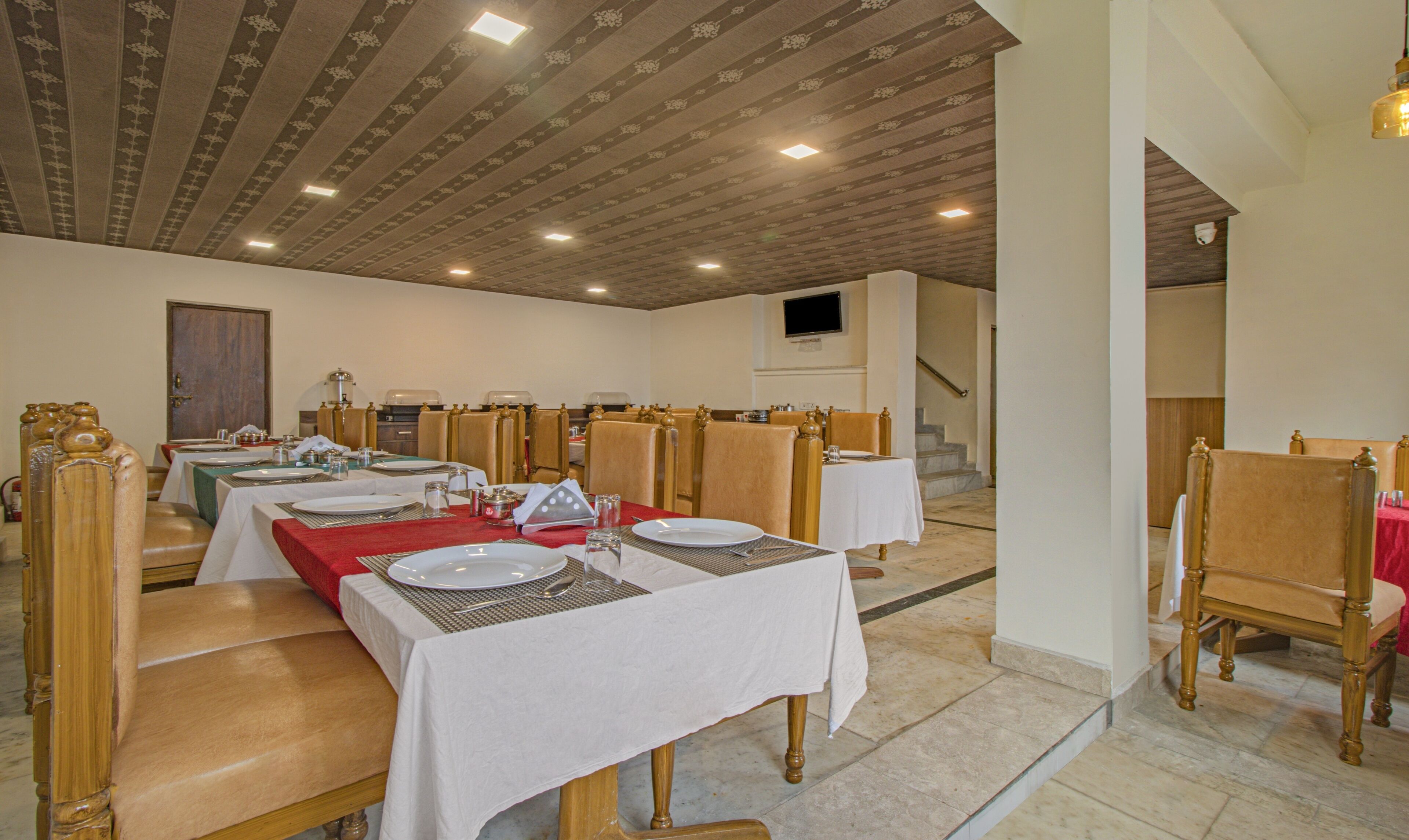 A dining area with tables set for service, wooden chairs, and a patterned ceiling.