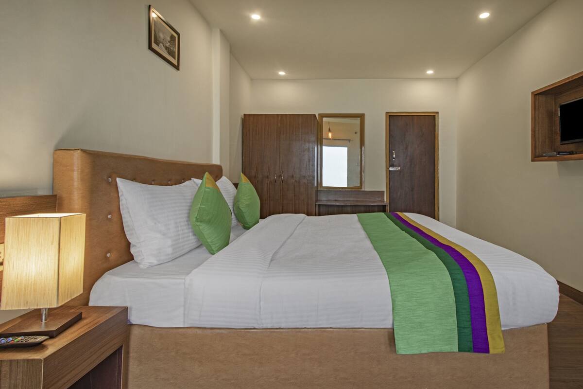A hotel room with a bed, a bedside lamp, a TV mounted on the wall, and a wooden wardrobe.