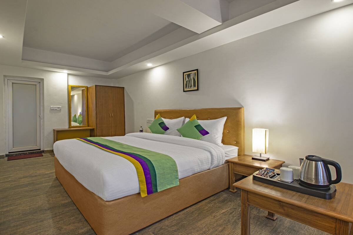 A hotel room with a bed, bedside table, lamp, and a coffee maker.