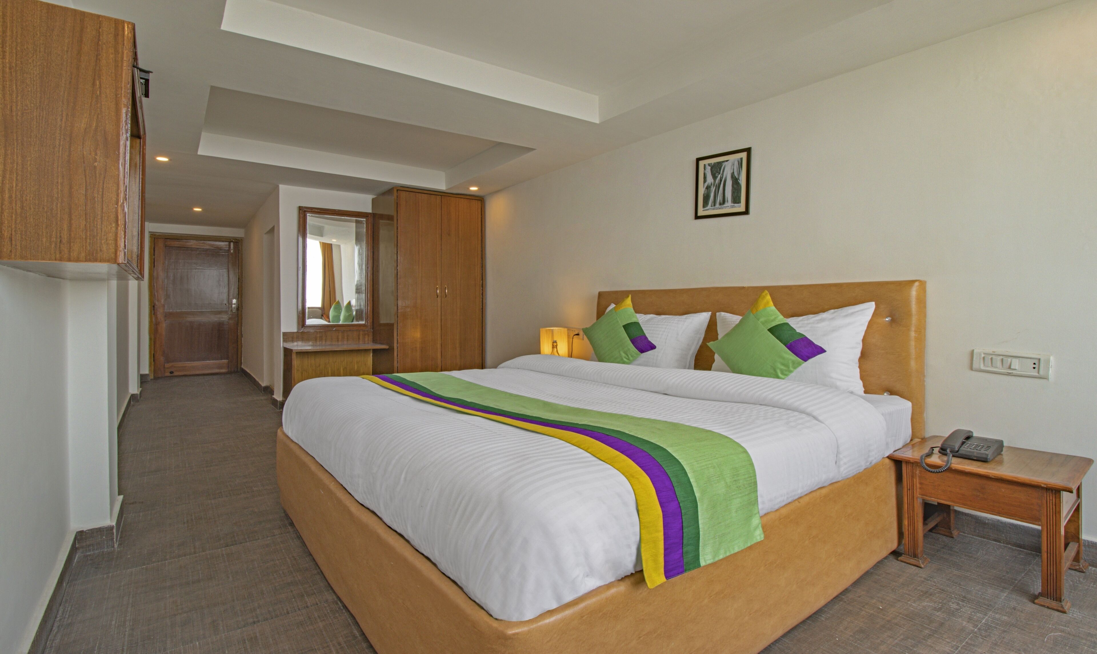Una camera d'albergo con un letto grande, una testiera in legno e un comodino con il telefono.