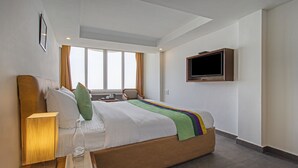Una habitación de hotel con una cama, un televisor fijado en la pared, una ventana con cortinas y una mesita de noche con una lámpara y un vaso.