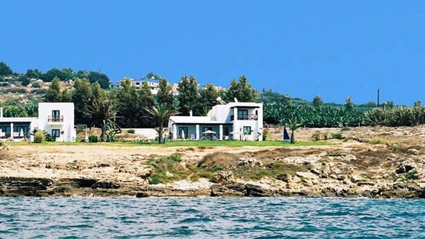 En fastighet belägen vid kusten, med vita byggnader, en stenstrand och en klarblå himmel.