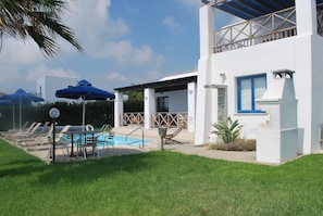 A modern building with a pool, lounge chairs, and umbrellas. - Sea Front Villa With Private Heated Pool, Quiet Area Paphos 322 (Kissonerga)