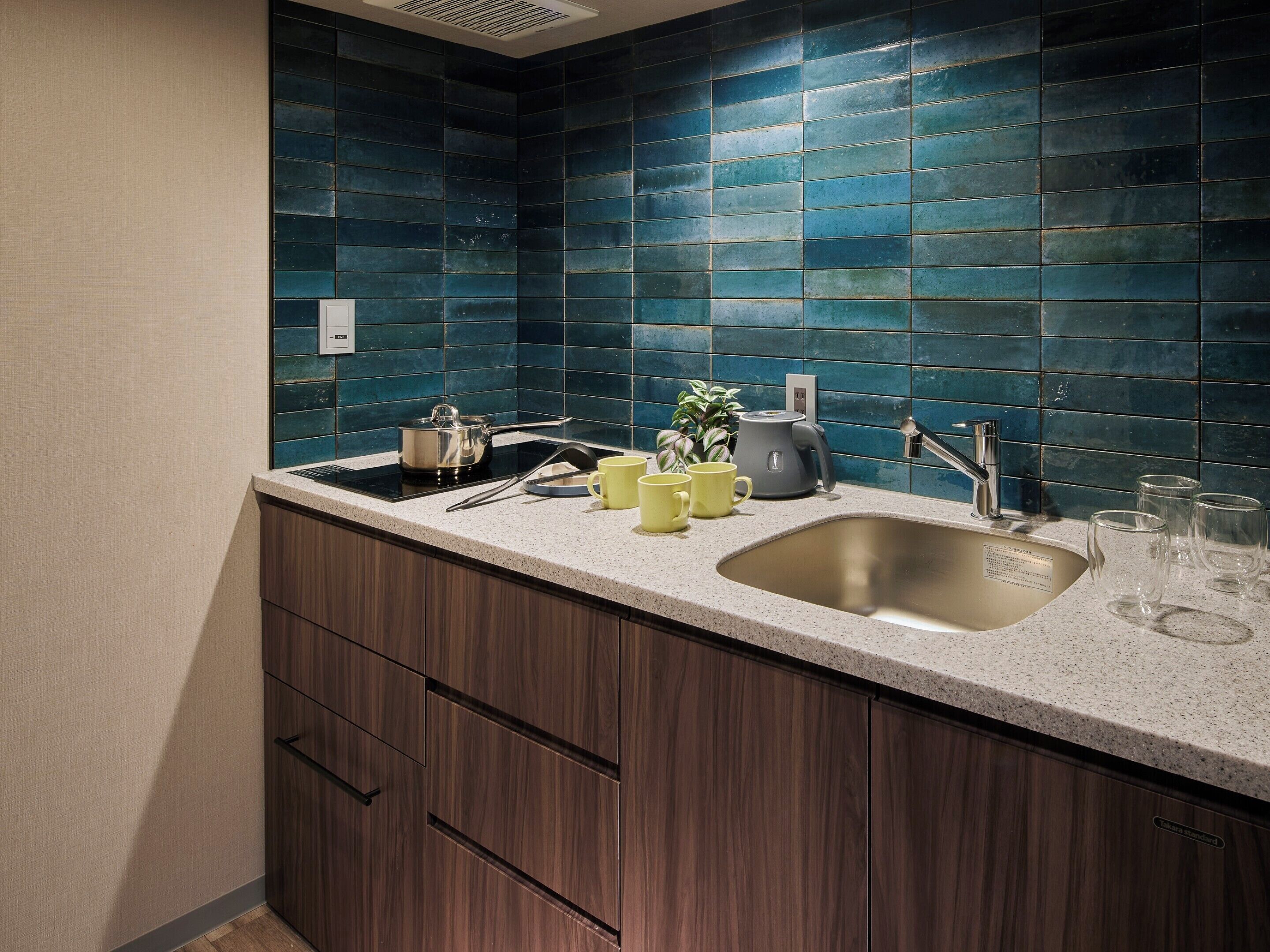 A kitchen with dark blue tiles, a stainless steel sink, and wooden cabinets.