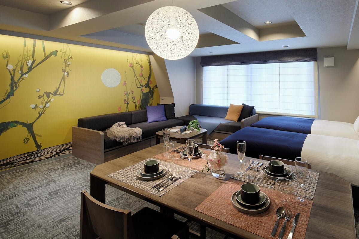 A modern hotel room with a dining area, a sofa, and a large window.