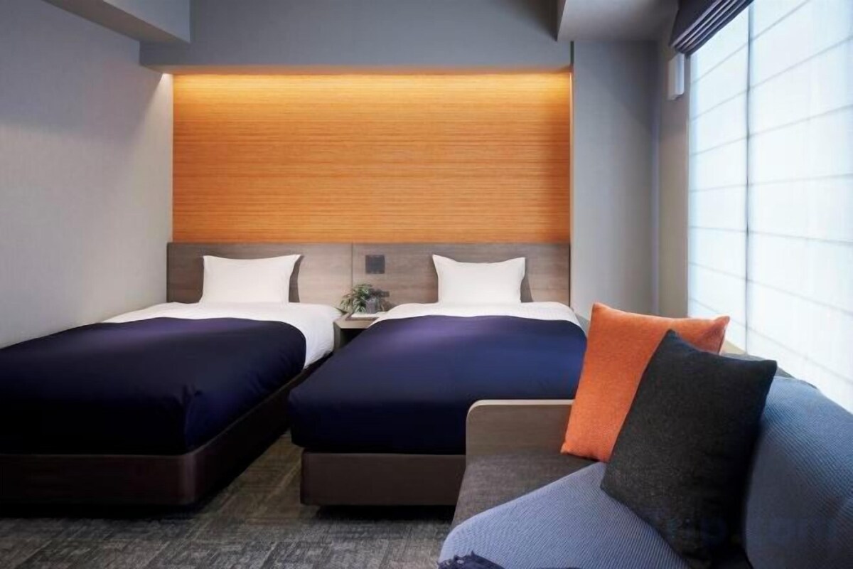 A hotel room with two beds, a sofa, and a nightstand with a lamp.