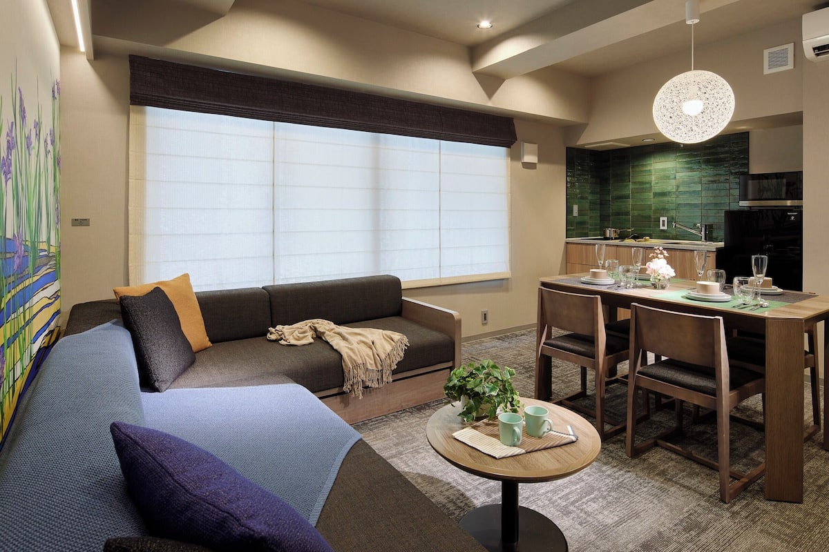 A modern living room with a sofa, a dining table, and a kitchen area.