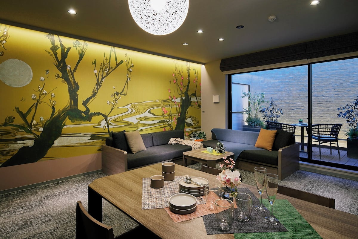 A modern living room with a dining area, featuring a large window, a wall mural, and a cozy seating arrangement.