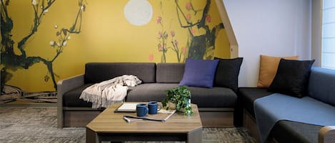 A cozy living room with a sofa, a coffee table, and a mural on the wall.