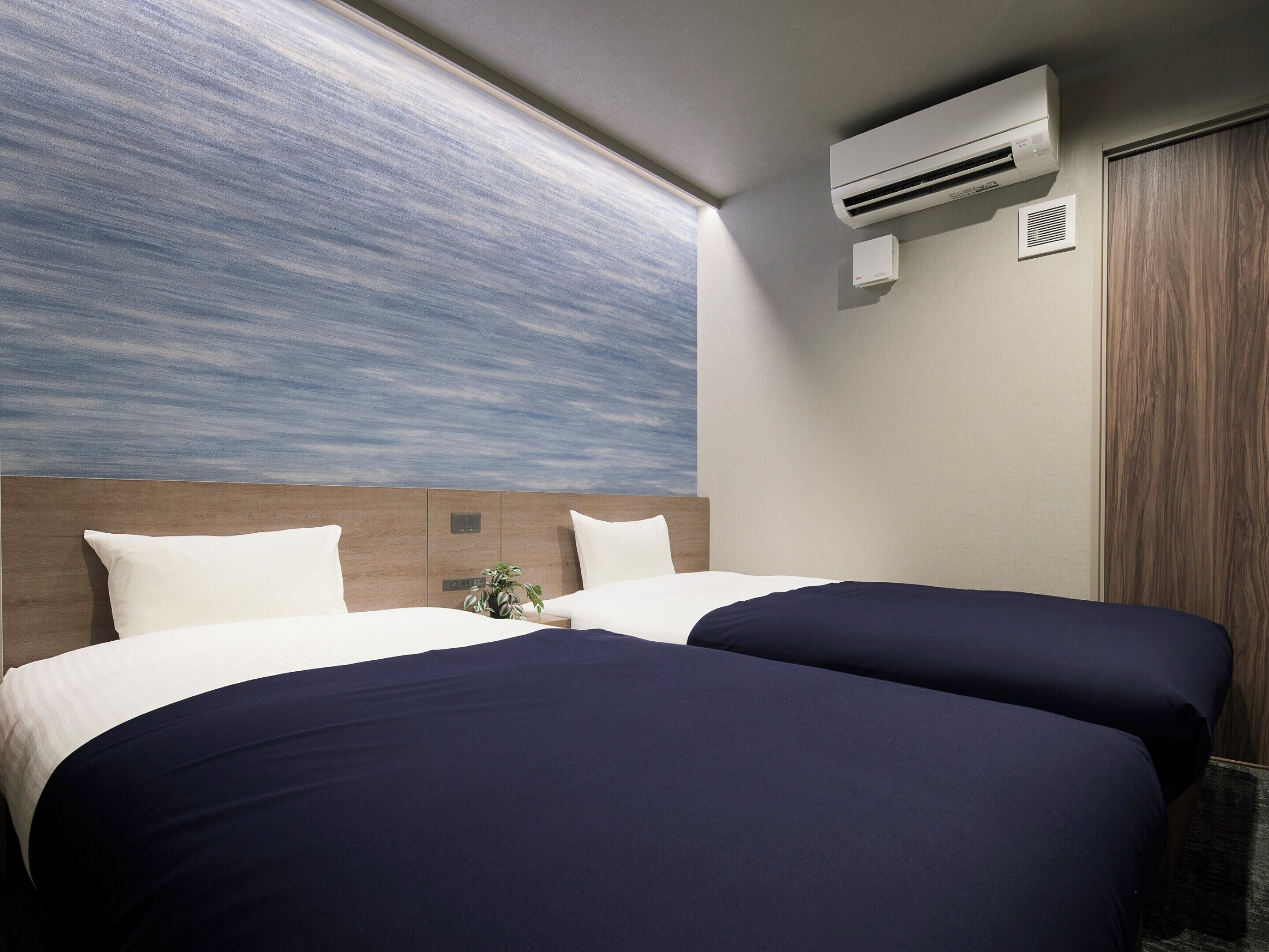 Habitación de hotel con dos camas, un ventanal con vistas, un aire acondicionado y una puerta de madera.
