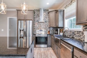 A modern kitchen with stainless steel appliances, a stone backsplash, and wooden cabinetry.