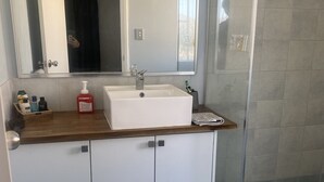A bathroom with a white sink, a mirror, and a shower area. - Self Contained Unit (Eaton)