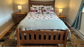 A bedroom with a wooden bed, two bedside tables with lamps, a patterned rug, and a framed picture on the wall. - Spacious Home on a Rushing Glacier Fed Creek (Seward)