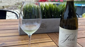 A wine bottle and glass on a wooden table outdoors.