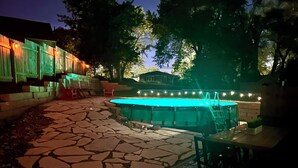 A stone patio leading to a swimming pool with a wooden deck and chairs.