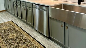 A modern kitchen with grey cabinets, a stainless steel dishwasher, and a large window with blinds.