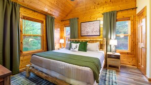 Une chambre à coucher dans un chalet en bois, avec un grand lit, deux tables de chevet avec des lampes et un tableau encadré au mur.