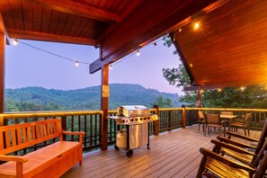 A wooden deck with a grill and seating area, overlooking a forested landscape. - Mountain Views! King beds, Hot Tub, Pool Table, Arcades, Private, Pool/Fish Pond (Sevierville)