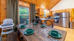 Une cabane en bois comprenant un coin repas aménagé pour quatre personnes, avec une chaise haute, et une cuisine équipée d’appareils électroménagers modernes.