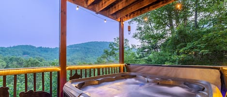 A hot tub on a wooden deck with a view of a forested hillside.