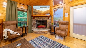 L’intérieur d’un chalet accueillant, avec une cheminée en pierre, deux fauteuils, une petite table et une vue sur l’extérieur par une fenêtre.