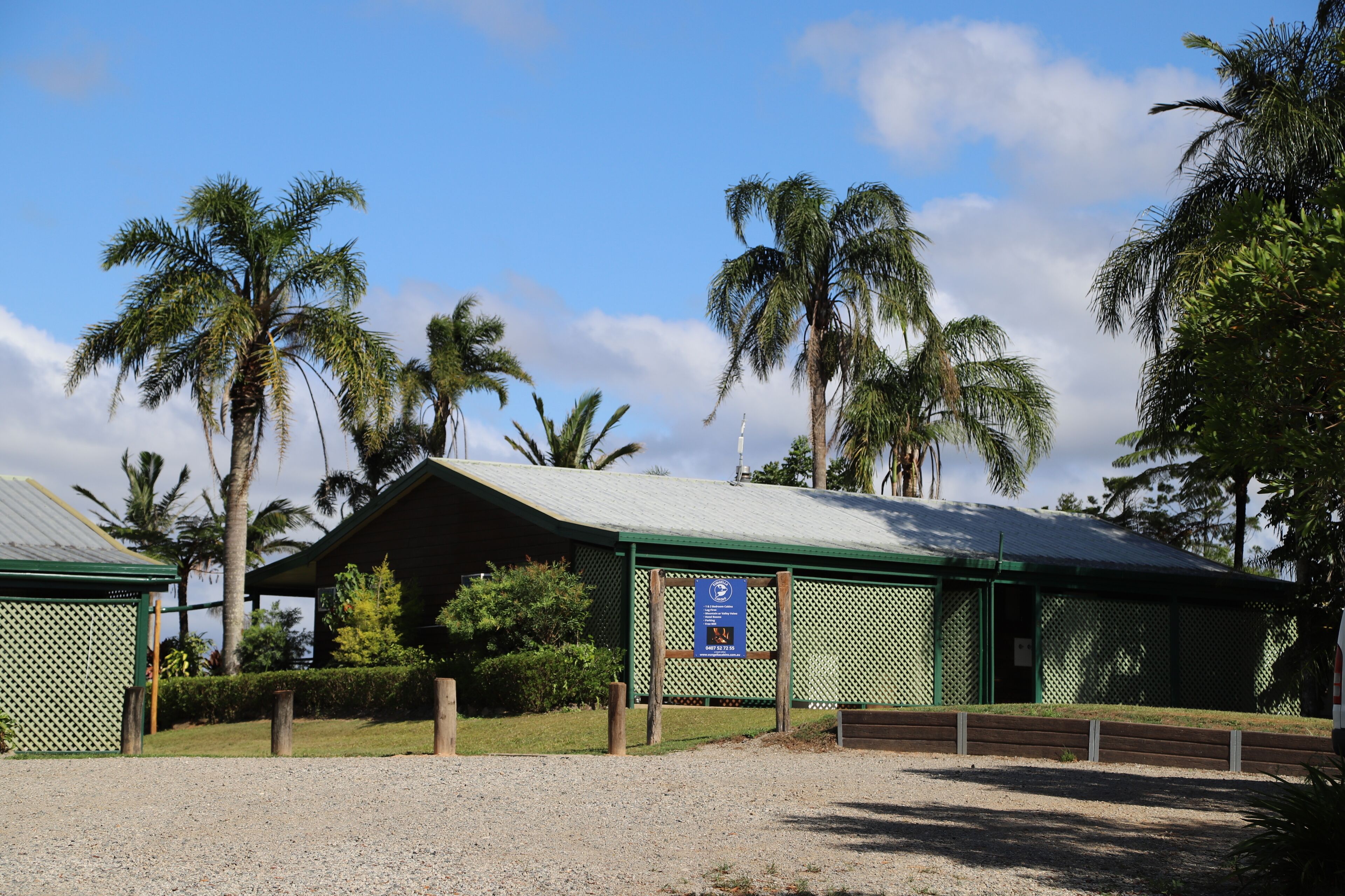 Un bâtiment doté d’un toit végétalisé et d’une enseigne bleue, entouré de palmiers et d’une zone recouverte de gravier.