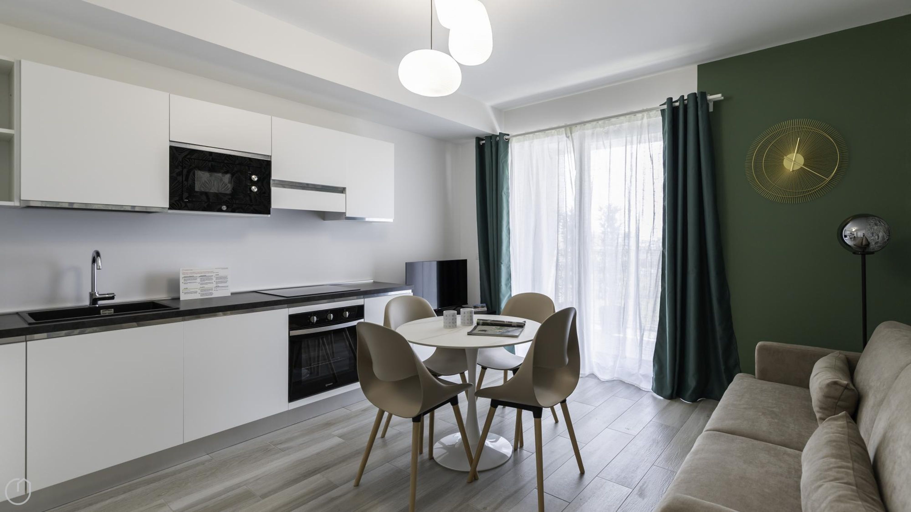 Una cocina moderna con armarios blancos, un microondas negro y una estufa. Hay una mesa de comedor con cuatro sillas y un televisor al fondo.