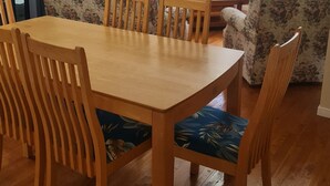 A dining area with a wooden table and chairs, a television, and floral-patterned sofas. - Private 2 Bedroom Granny Flat. Sleeps 5, Pets Welcome (Darra)