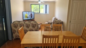 A living room with a TV, floral sofa, wooden dining table, and chairs. - Private 2 Bedroom Granny Flat. Sleeps 5, Pets Welcome (Darra)