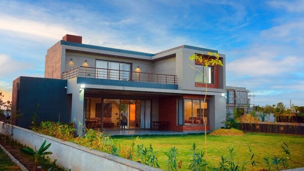 Une maison moderne à deux étages, dotée d’un toit plat, de grandes fenêtres et d’un balcon.