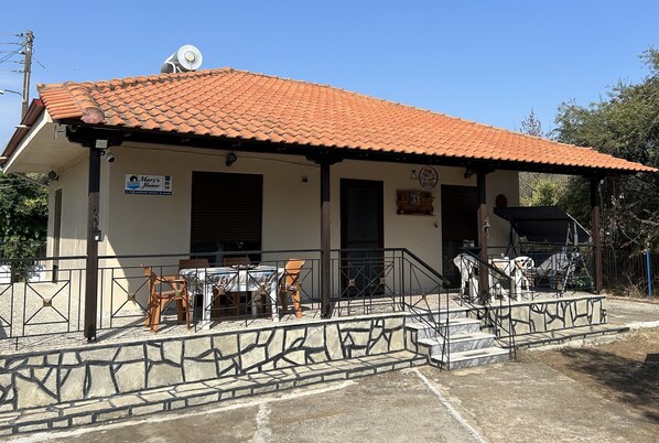 A building with a tiled roof, a sign reading "Man's House," outdoor seating with chairs and tables, and a staircase leading to the entrance.