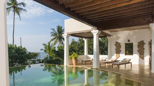 A poolside area with lounge chairs, a pergola, and a view of the ocean. - Saffron House in Weligama (Weligama)