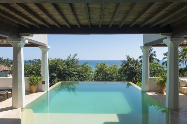 A rectangular pool with a clear view of the ocean and palm trees in the background.